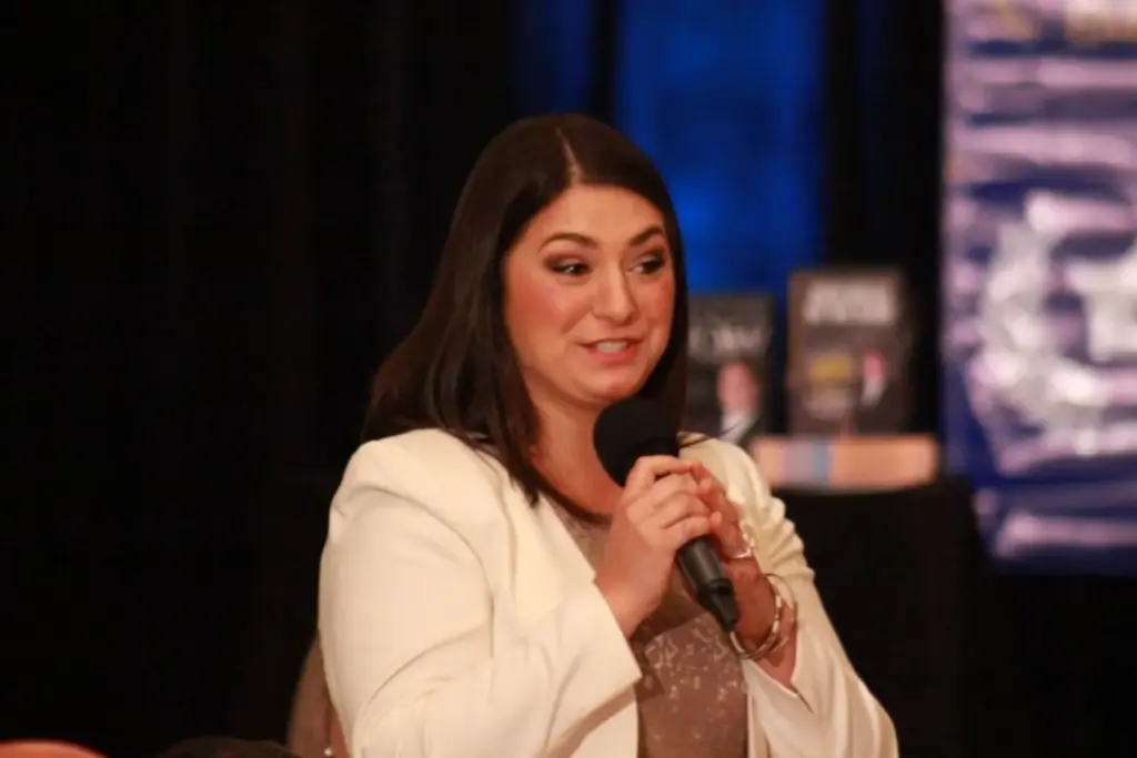 Sonia Gomez speaking confidently into a microphone at an event, engaging the audience with impactful communication and leadership insights.