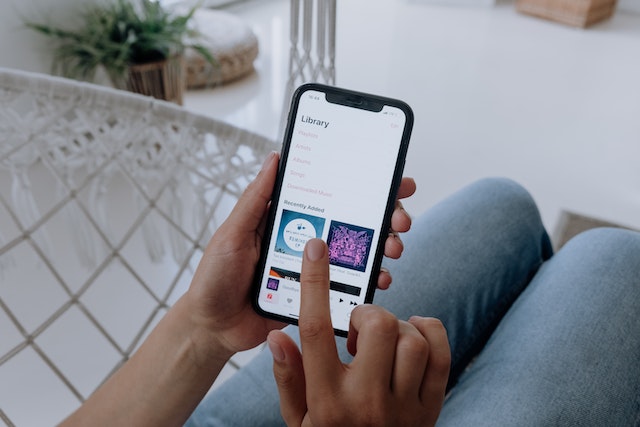 Person using smartphone to browse music library, featuring recently added tracks, in a cozy indoor setting.